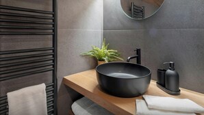 Un baño moderno con un espejo redondo, lavabo negro y una pequeña planta en maceta.