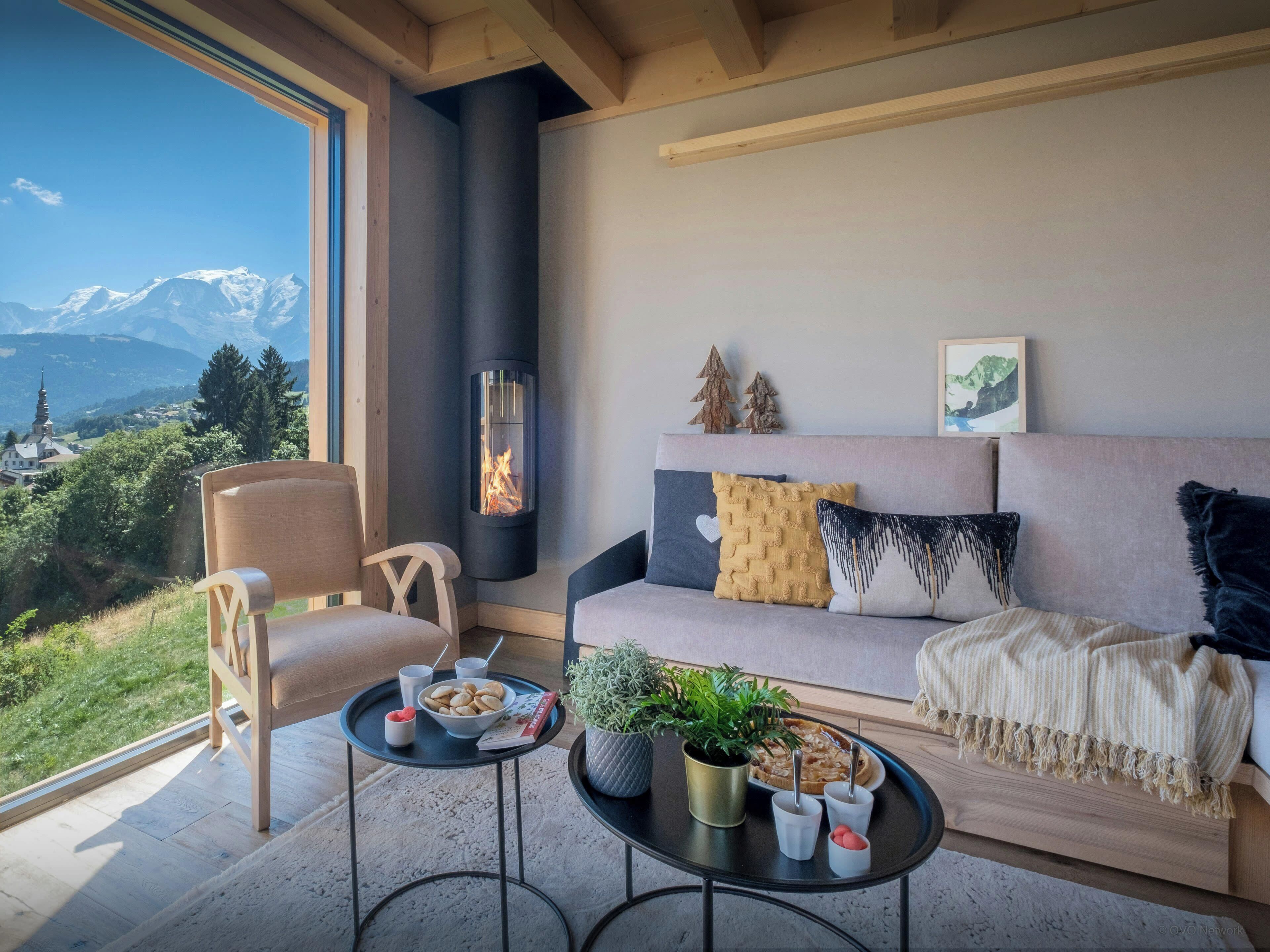 A cozy living room with a sofa, a chair, a fireplace, a view of mountains, and a dining table with snacks.