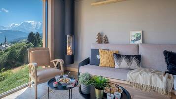 A cozy living room with a sofa, a chair, a fireplace, a view of mountains, and a dining table with snacks.