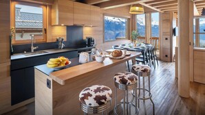 Una cocina moderna con vigas de madera, una isla grande con taburetes y vistas a montañas a través de amplios ventanales.