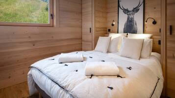 A wooden-paneled bedroom with a large bed, white bedding, a framed deer picture, and a window with a view of greenery.