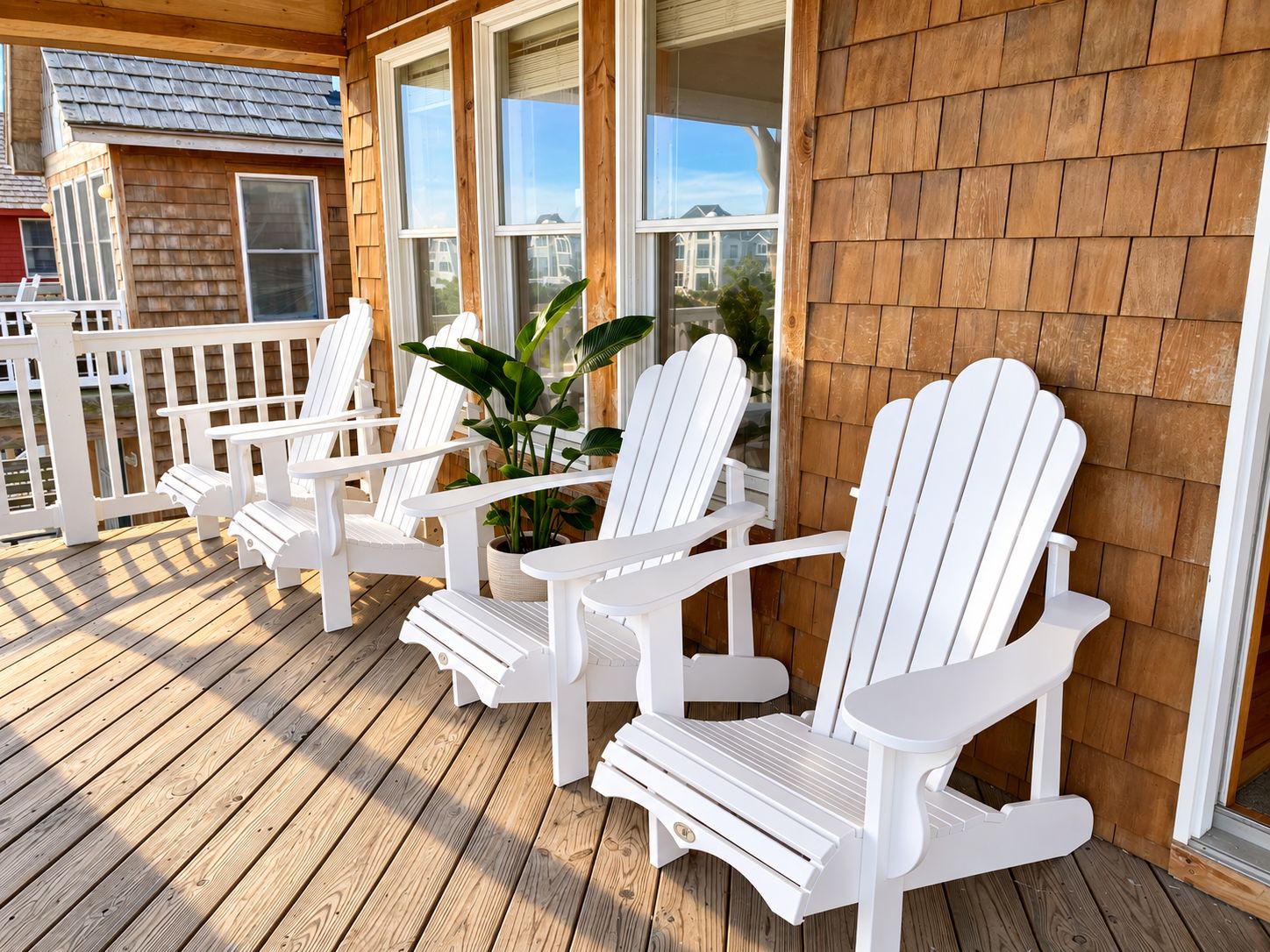 A wooden deck with white Adirondack chairs and a potted plant.