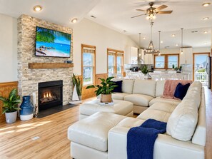A spacious living room with a fireplace, a large sectional sofa, and a television mounted on a stone wall.