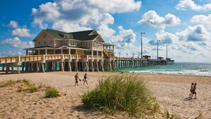 Ein Strandhaus mit einem Steg, der ins Meer führt, mit mehreren Etagen und einem Balkon.