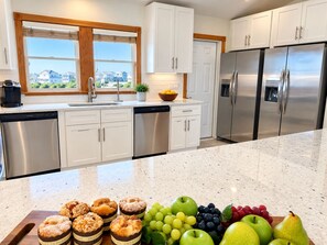 A modern kitchen with stainless steel appliances, white cabinetry, and a large window offering a view of the neighborhood.