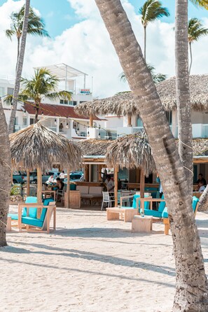 Een strandresort met rieten parasols, houten meubels en palmbomen.
