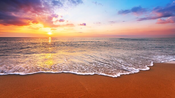 Une plage avec un coucher de soleil sur l’océan.
