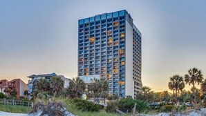 Un hôtel de grande hauteur doté de nombreux balcons, entouré de palmiers et de la végétation typique des plages.