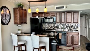 Une cuisine moderne avec des meubles en bois, un réfrigérateur noir, un évier en acier inoxydable et un coin bar avec des tabourets.