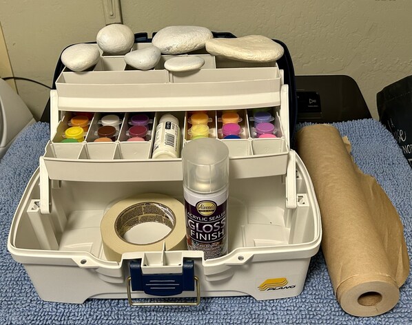 A storage box with compartments containing paint containers, a bottle of acrylic sealer, and a roll of brown paper. - Unwind and Relax at Hidden Trails Retreat (Payson)