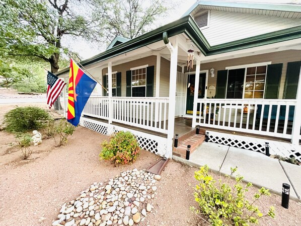 A building with a white porch, a flag, and a small garden. - Unwind and Relax at Hidden Trails Retreat (Payson)