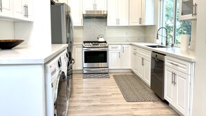 Una cocina moderna con armarios blancos, electrodomésticos de acero inoxidable y un amplio ventanal que proporciona luz natural.