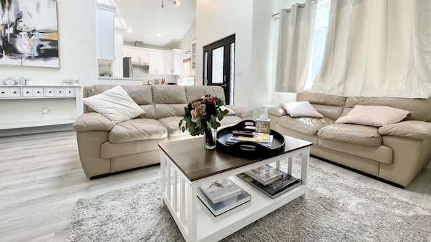 Una sala de estar moderna con dos sofás color beige, una mesa de centro de vidrio y una alfombra blanca.
