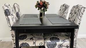Una mesa de comedor con un florero, rodeada de sillas con estampado, y pinturas abstractas en la pared.