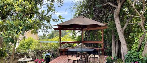 A wooden deck with a gazebo, a round table, and chairs.