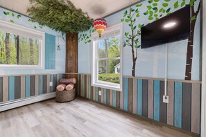 A room with wooden paneling, a large window, a television, and a decorative tree mural. - Room for the whole family 1/2 hour to Mohegan and Mystic Seaport (Colchester)