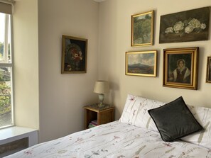 A bedroom with a bed, a nightstand, and a window. There are four framed pictures on the wall. - Six on Castle (Tiverton)