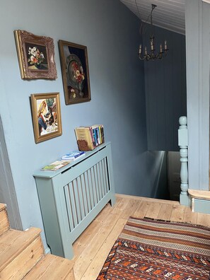 A room with a light blue wall, a wooden floor, a patterned rug, a blue radiator, and three framed pictures. - Six on Castle (Tiverton)