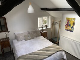 A bedroom with a bed, a hanging light fixture, a window, a radiator, and a poster on the wall.