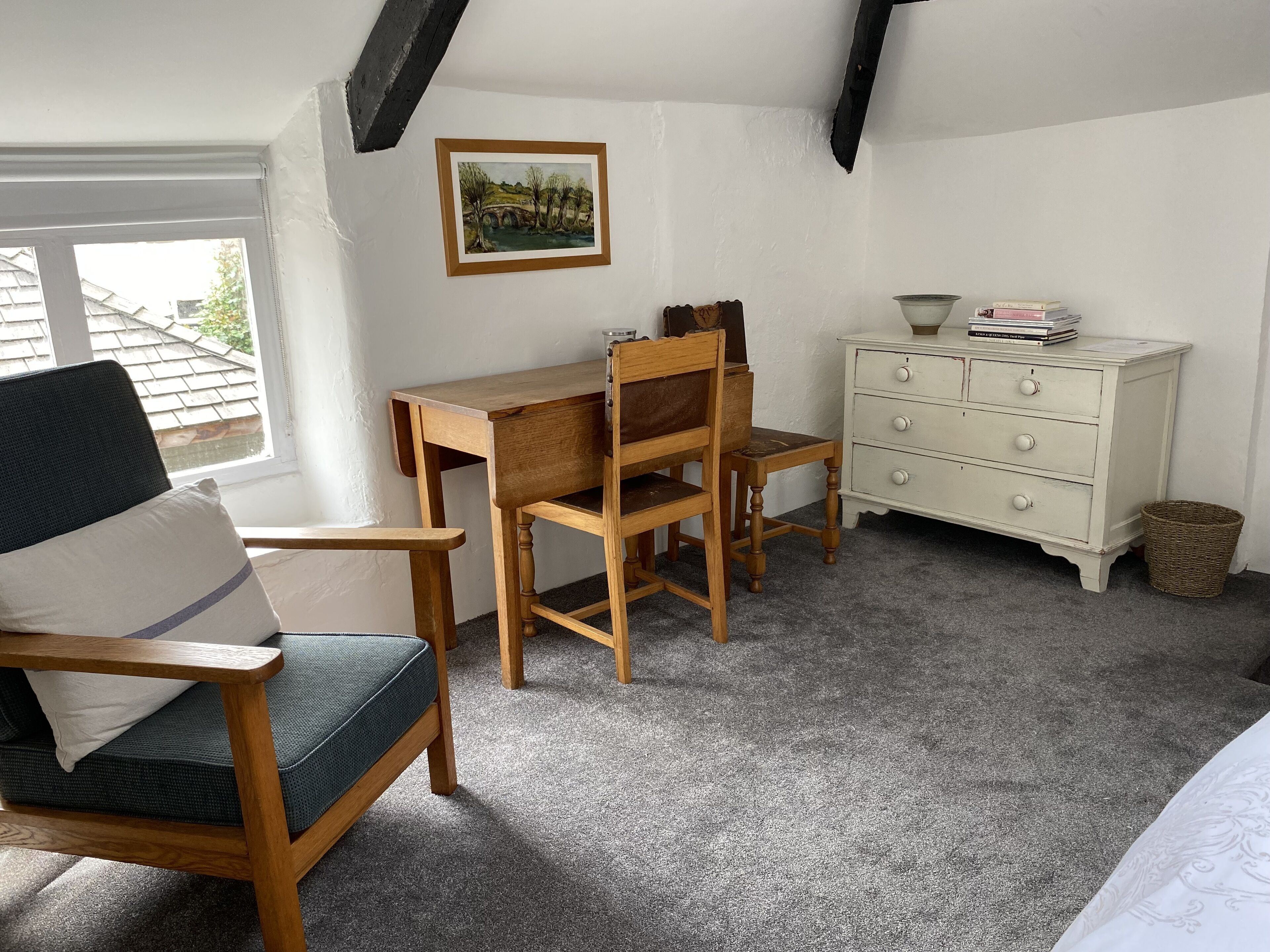 Une pièce confortable avec un bureau en bois, une chaise, une commode et une fenêtre donnant sur une maison.