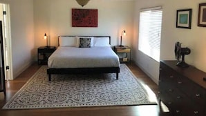 Ein Schlafzimmer mit einem Bett, zwei Nachttischen, einem Deckenventilator, einem Fenster mit Jalousien und einem Schminktisch.