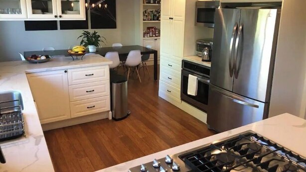 Eine moderne Küche mit weißen Schränken, einem Edelstahl-Kühlschrank, einem Gasherd und einem Essbereich mit Tisch und Stühlen.