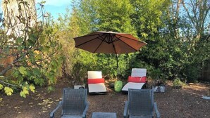 Ein Sitzbereich im Freien mit zwei Stühlen, einem Tisch, einem Sonnenschirm und einem Stuhl mit rotem Kissen.