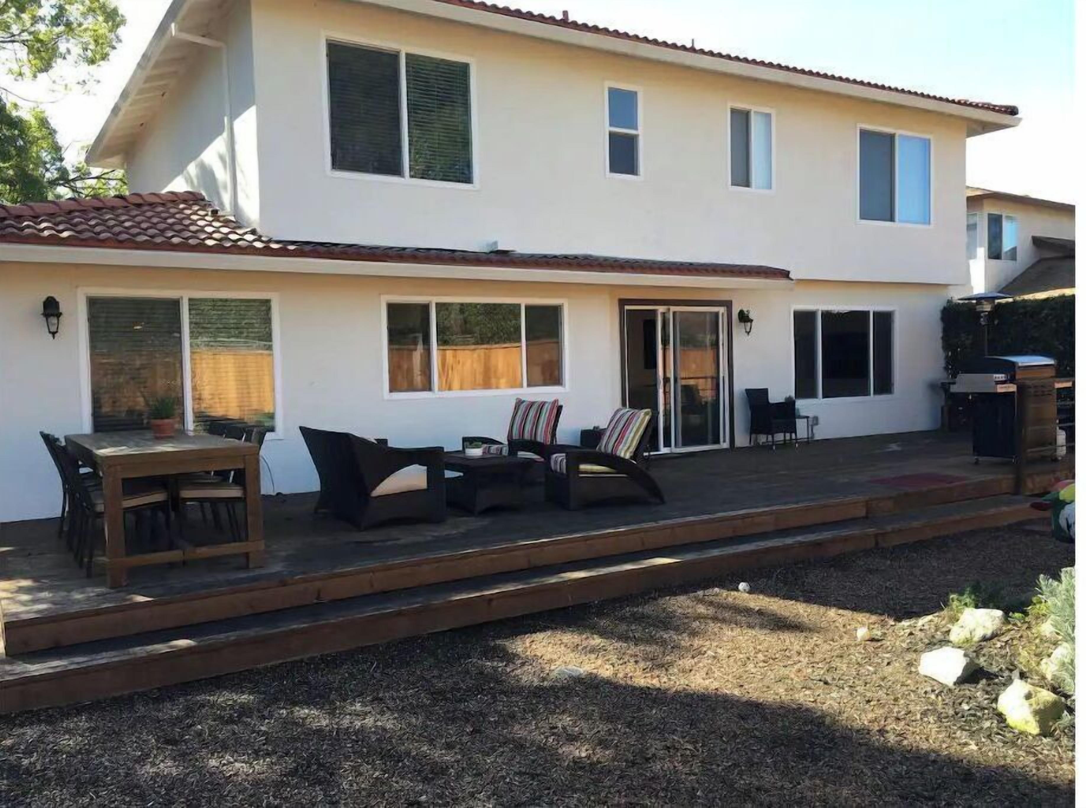 A two-story house with a patio area featuring outdoor furniture and a barbecue grill.