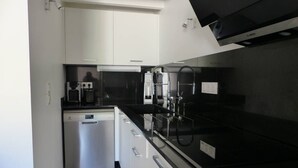 Uma cozinha compacta com armários brancos, bancada preta e lava-louças Bosch.