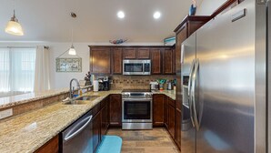 Una cocina con encimeras de granito, electrodomésticos de acero inoxidable, armarios de madera y una alfombra azul.
