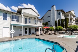 A swimming pool area with lounge chairs and a red umbrella, surrounded by multi-story buildings with balconies.
