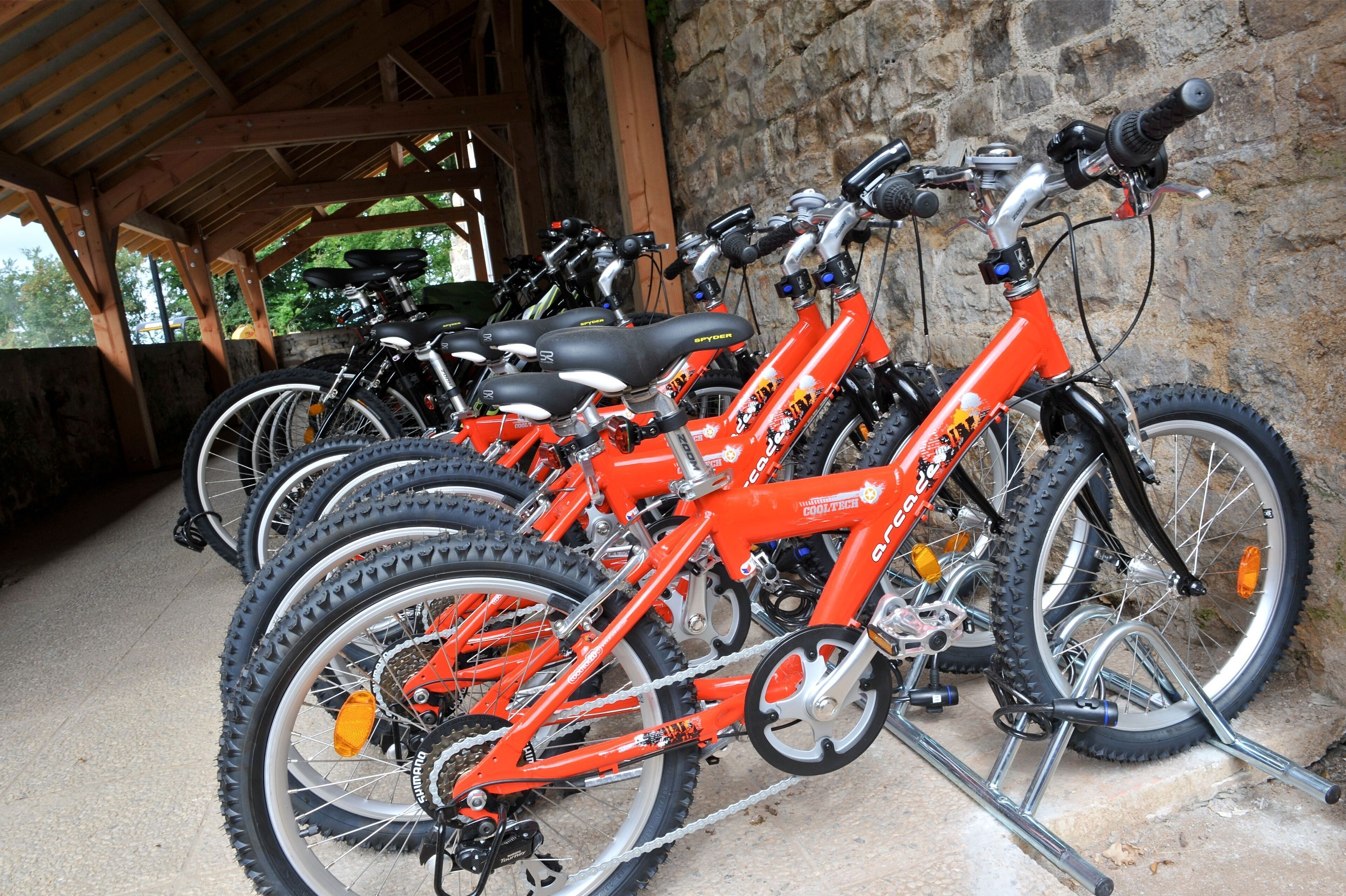 A row of orange mountain bikes parked under a wooden shelter.