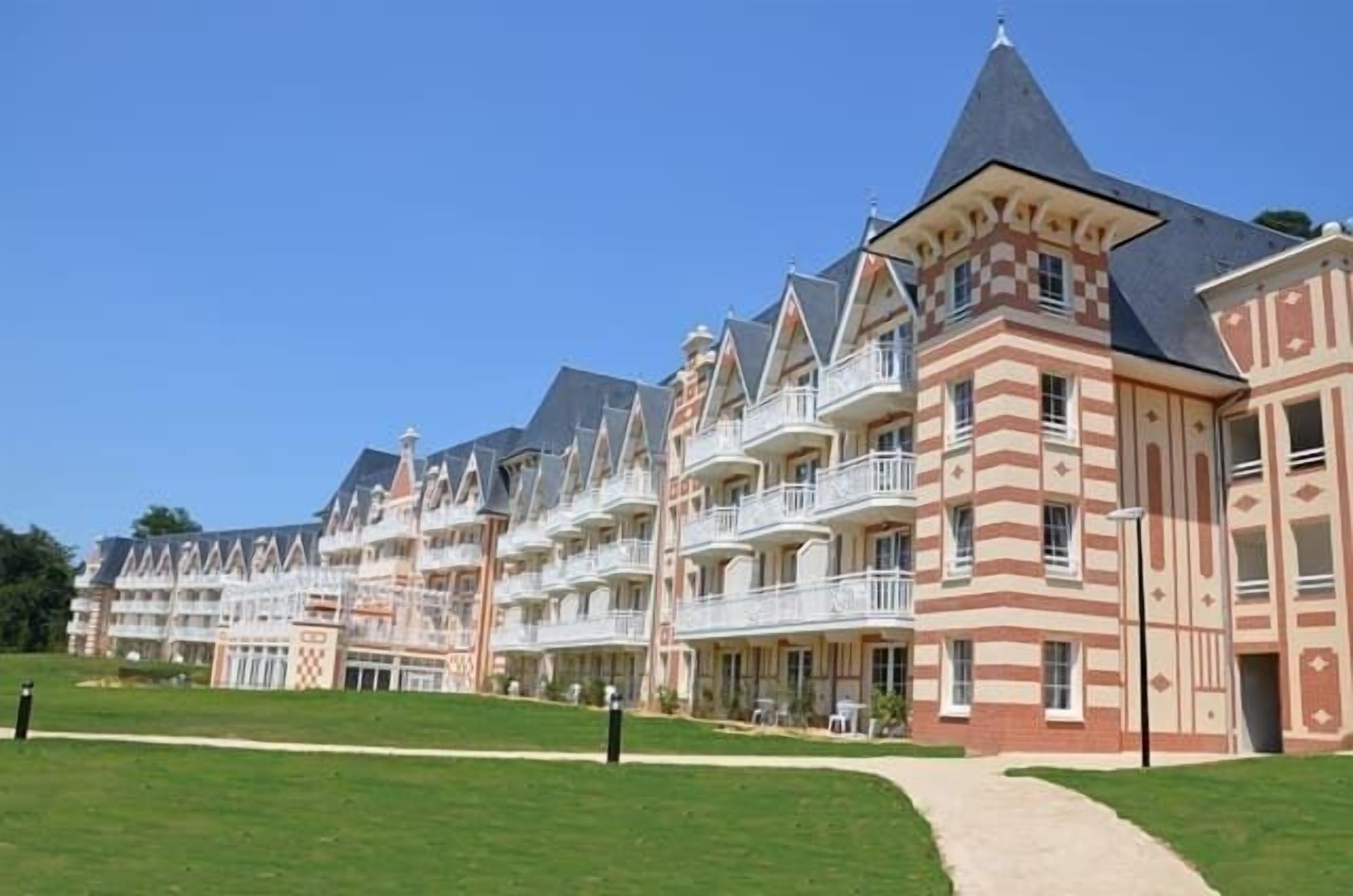 Une rangée d’immeubles à étages avec des balcons, un chemin central et une pelouse bien entretenue.