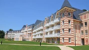 Une rangée d’immeubles à étages avec des balcons, un chemin central et une pelouse bien entretenue.