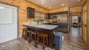 A modern kitchen with wooden paneling, a central island with stools, stainless steel appliances, and a large window.