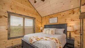 A wooden cabin bedroom with a bed, two bedside tables, and a window with blinds.