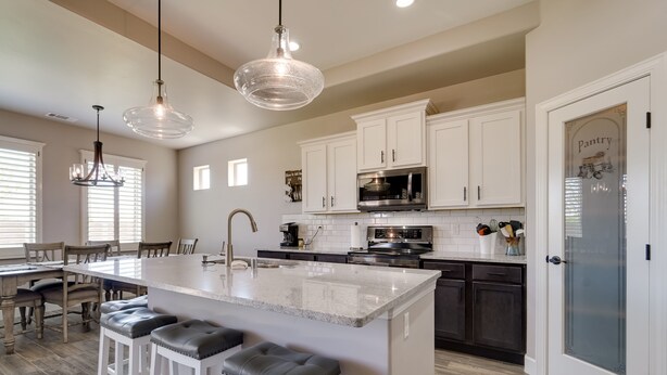 Una cocina moderna con armarios blancos, una isla grande con taburetes de bar, electrodomésticos de acero inoxidable e iluminación colgante.