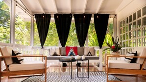 A sunlit room with a sofa, two chairs, a small table, and a patterned rug. - La Prometida Hotel (Cahuita)