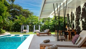 A poolside area with lounge chairs, a wooden table, and a pergola. - La Prometida Hotel (Cahuita)