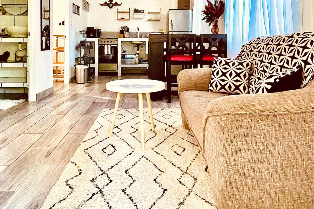 A spacious living room with a ceiling fan, a dining area with a table and chairs, and a kitchen in the background.