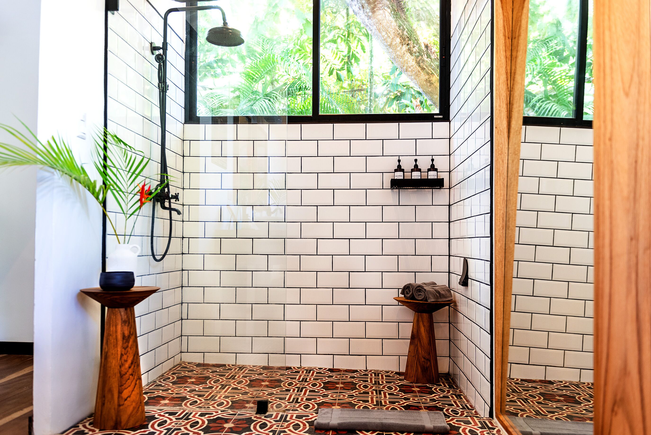 Un baño moderno con paredes de azulejos blancos, piso estampado y zona de ducha con vistas a la vegetación.