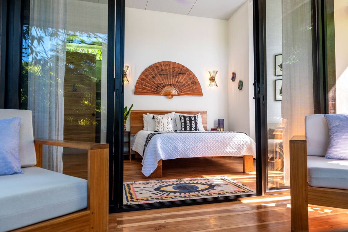 A bedroom with a bed, a wooden headboard, a wall-mounted fan, and two bedside lamps.