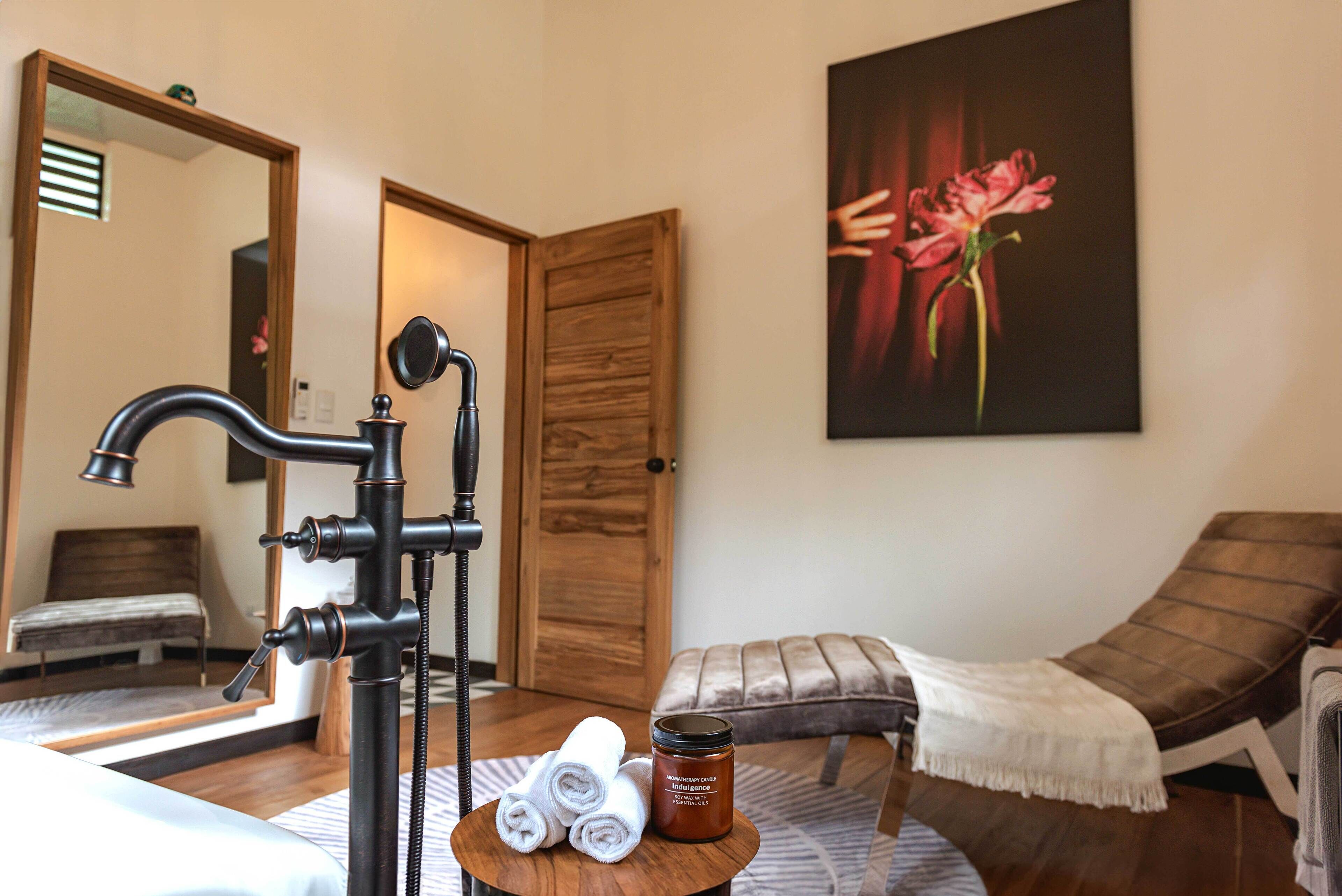 A spa room with a massage table, a wooden door, a mirror, and a painting of a flower.