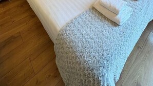 Un lit bien fait, avec du linge de lit blanc et une tête de lit grise, une petite table de chevet et un tableau de fleurs accroché au mur.