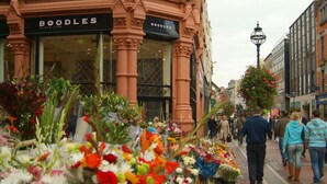 Une rue où se trouve un marché aux fleurs et un bâtiment portant l’enseigne « BOODLES ».