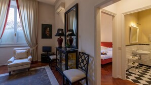 Hotelkamer met een bed, bureau met een computer, stoel, bank, raam met gordijnen, spiegel en een badkamer met wastafel en betegelde vloer.