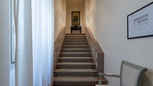 A staircase with a marble railing, a framed picture on the wall, and a chair to the right.
