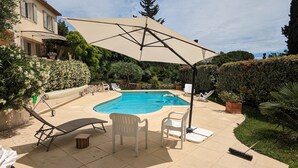 Ein Pool mit Liegestühlen und einem großen Sonnenschirm, umgeben von gepflegten Hecken und Bäumen.