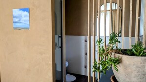 Ein Badezimmer mit Toilette, Waschbecken und Spiegel. Auf einem Tisch steht eine Topfpflanze.