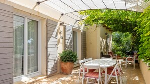 Eine überdachte Terrasse mit Tisch, Stühlen und einem Blumentopf, sowie eine Glastür.